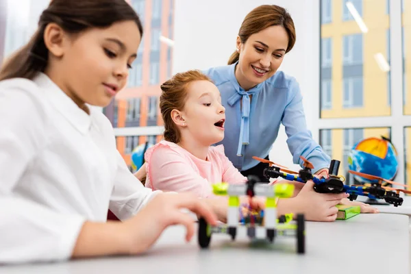 Insegnante sorridente in piedi vicino agli alunni con giocattoli educativi in classe — Foto stock