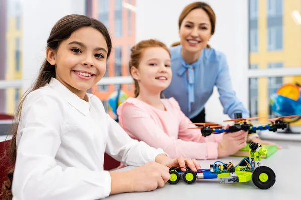 Insegnante sorridente in piedi vicino agli alunni con giocattoli educativi in classe — Foto stock