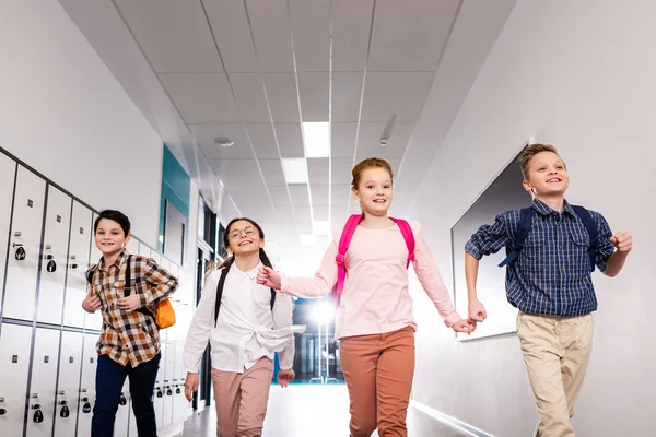Cuatro alumnos emocionados con mochilas corriendo corredor después de clases - foto de stock