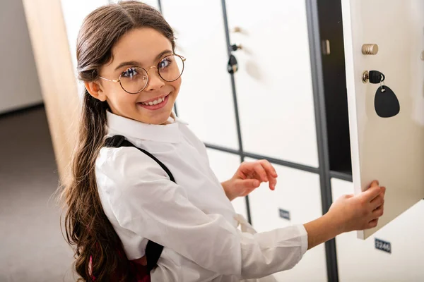 Lachende Schülerin mit Brille steht während der Pause in der Schule neben Schließfächern — Stockfoto