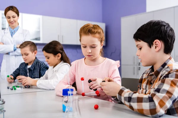 Alunos concentrados segurando estruturas moleculares enquanto estavam sentados em sala de aula durante a aula de química — Fotografia de Stock