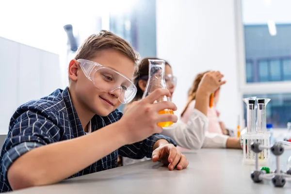 Ученики в защитных очках держат стаканы во время урока химии — стоковое фото