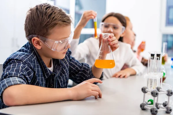 Alumnos con gafas protectoras sosteniendo vasos de precipitados durante la lección de química - foto de stock