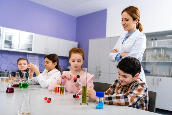 Alumnos sosteniendo estructuras moleculares mientras están sentados en el aula durante la lección de química - foto de stock