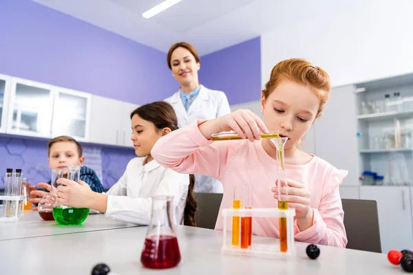 Alumnos con frascos haciendo experimento químico durante la lección de química - foto de stock