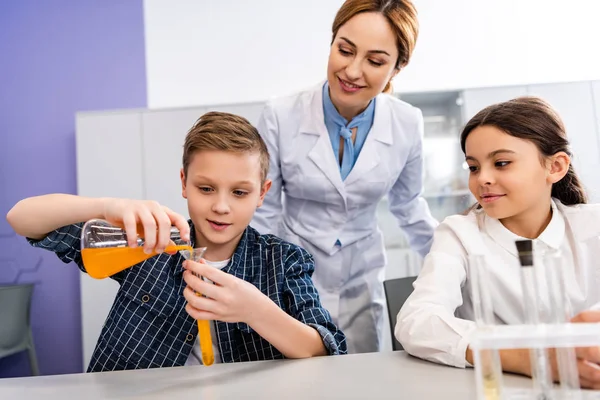 Учитель химии смотрит на ученика с мензуркой и фляжкой в классе — стоковое фото