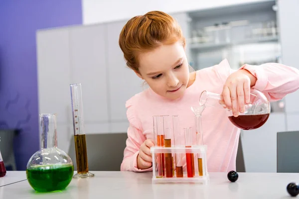 Smiling schoolgirl holding beaker and doing chemical experiment during chemistry lesson — Stock Photo