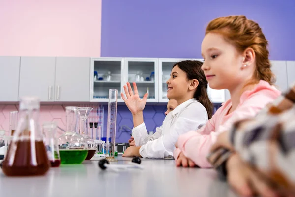 Smiling schoolgirl raising hand in class during chemistry lesson — Stock Photo