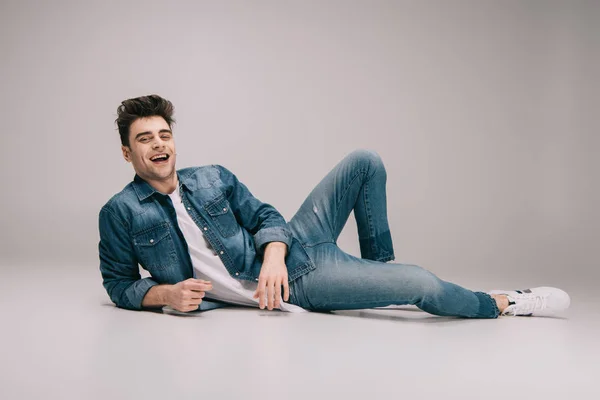 Uomo sorridente e bello in jeans, gonna e t-shirt sdraiato sul pavimento e guardando la fotocamera — Foto stock