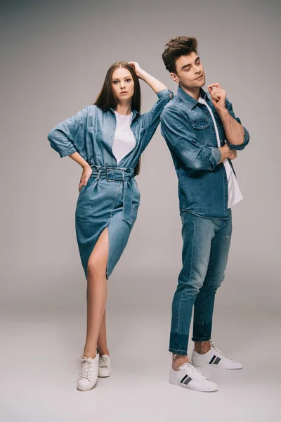 Hermosa novia en vestido de mezclilla y novio guapo en jeans y camisa sobre fondo gris - foto de stock