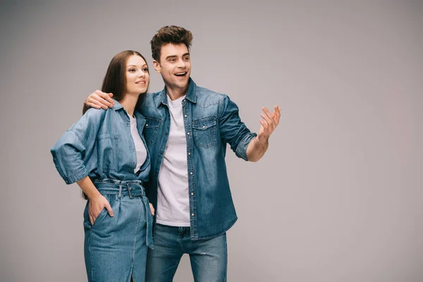 Привлекательная девушка в джинсовом платье и парень в джинсах и рубашке обнимает и смотрит в сторону — стоковое фото
