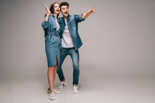 Surprised girlfriend in denim dress and smiling boyfriend in jeans and shirt pointing with finger — Stock Photo