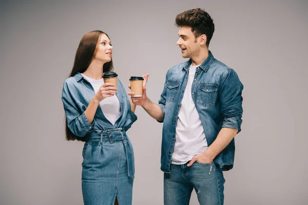 Girlfriend in denim dress and smiling boyfriend in jeans and shirt holding paper cups and talking — Stock Photo