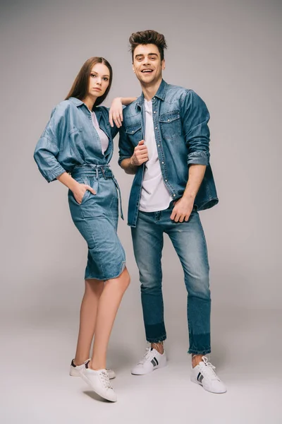 Girlfriend in denim dress with hand in pocket and smiling boyfriend in jeans and shirt looking at camera — Stock Photo