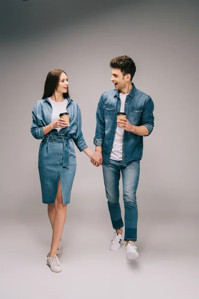 Namorada em vestido de ganga e namorado bonito em jeans e camisa segurando copos de papel e de mãos dadas — Fotografia de Stock