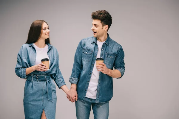 Girlfriend in denim dress and handsome boyfriend in jeans and shirt holding paper cups looking at each other — Stock Photo