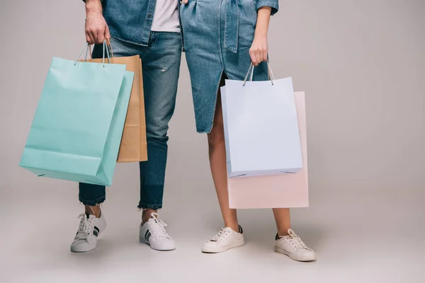Vista cortada de homem e mulher segurando sacos de compras em fundo cinza — Fotografia de Stock