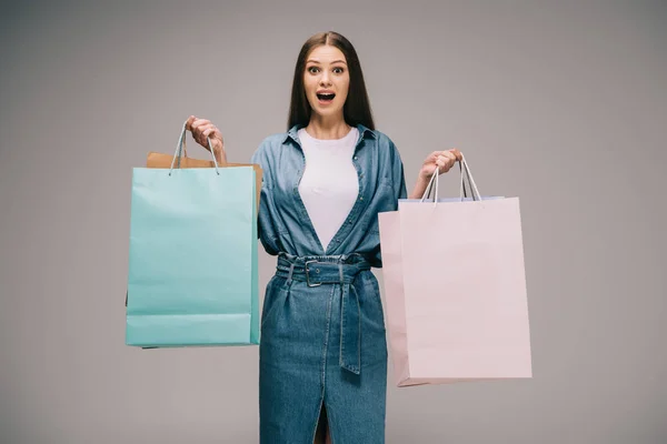 Überraschte und schöne Frau im Jeanskleid mit Einkaufstaschen und Blick in die Kamera — Stockfoto