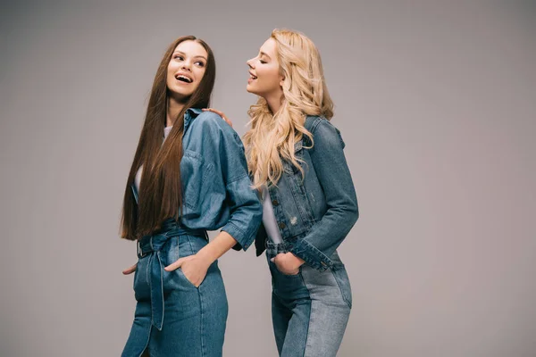 Blonde and brunette women in denim clothes smiling on grey background — Stock Photo