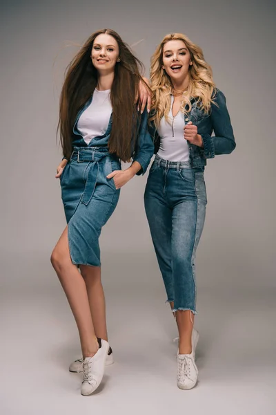 Femme brune heureuse avec les mains dans les poches et femme blonde en vêtements en denim souriant et regardant la caméra — Photo de stock