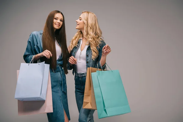 Happy blonde and brunette women in denim clothes smiling and holding shopping bags — Stock Photo