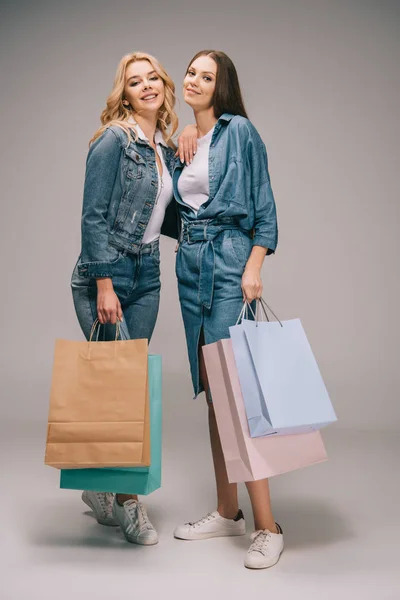 Schöne blonde und brünette Frauen in Jeanskleidung, die Einkaufstüten in der Hand halten und in die Kamera schauen — Stockfoto