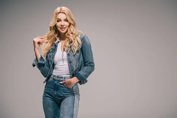 Attraktive blonde Frau in Jeanskleidung, die Hand in der Tasche, lächelnd und in die Kamera blickend — Stockfoto