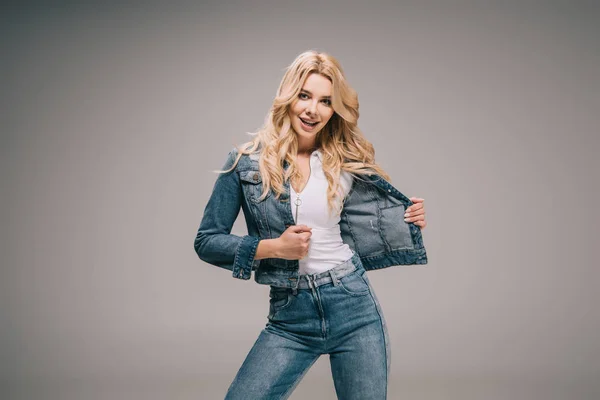 Attraktive blonde Frau in Jeansjacke und Jeans, die lächelt und in die Kamera schaut — Stockfoto