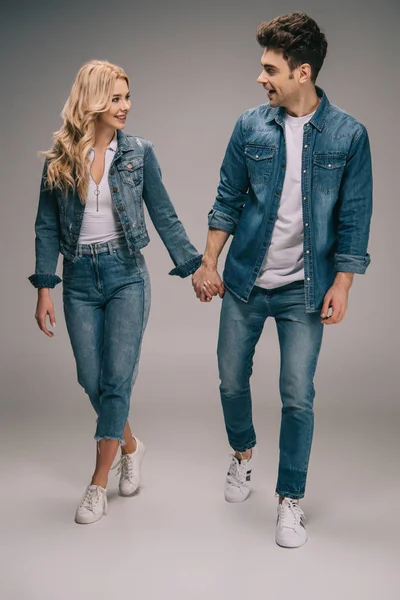 Namorado feliz e namorada sorridente em roupas jeans de mãos dadas e olhando um para o outro — Fotografia de Stock
