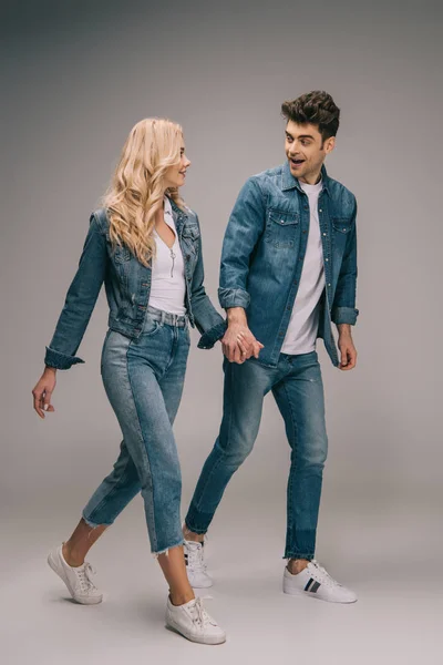 Namorado surpreso e namorada atraente em roupas jeans de mãos dadas e olhando um para o outro — Fotografia de Stock