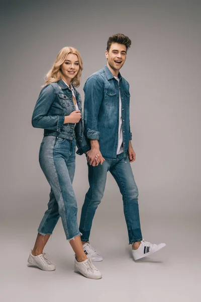 Novio sonriente y atractiva novia en ropa de mezclilla cogidas de la mano y mirando a la cámara - foto de stock