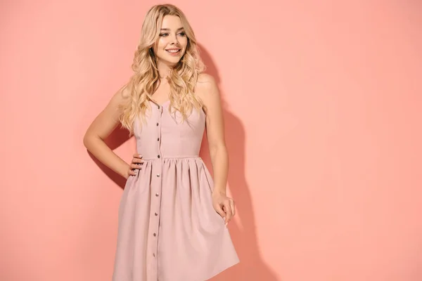 Blonde and beautiful woman with hand on hip in pink dress smiling and looking away — Stock Photo