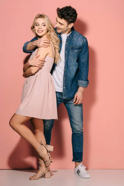 Smiling girlfriend in pink dress and handsome boyfriend in denim shirt hugging — Stock Photo