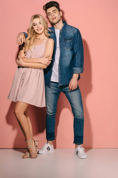 Novia sonriente en vestido rosa y novio guapo en camisa de mezclilla abrazando y mirando a la cámara - foto de stock