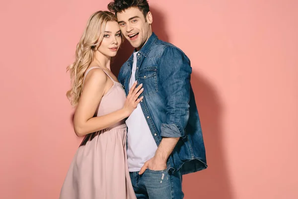 Freundin im rosa Kleid und schöner Freund im Jeanshemd umarmen sich und schauen in die Kamera — Stockfoto