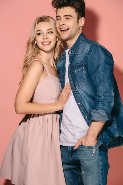 Sorrindo namorada em vestido rosa e namorado bonito em camisa jeans abraçando e olhando para longe — Fotografia de Stock