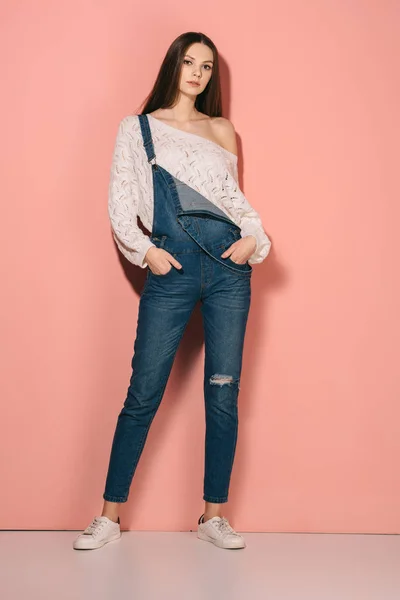 Brunette and beautiful woman in denim overalls with hands in pockets looking at camera — Stock Photo