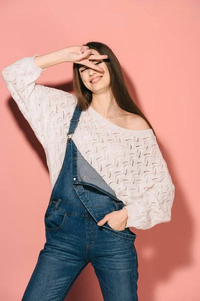 Brünette und schöne Frau in Jeans-Overalls, die Friedenszeichen zeigt und lächelt — Stockfoto