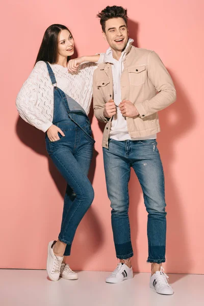 Morena e bela namorada em macacão jeans e namorado bonito sorrindo e olhando para longe — Fotografia de Stock