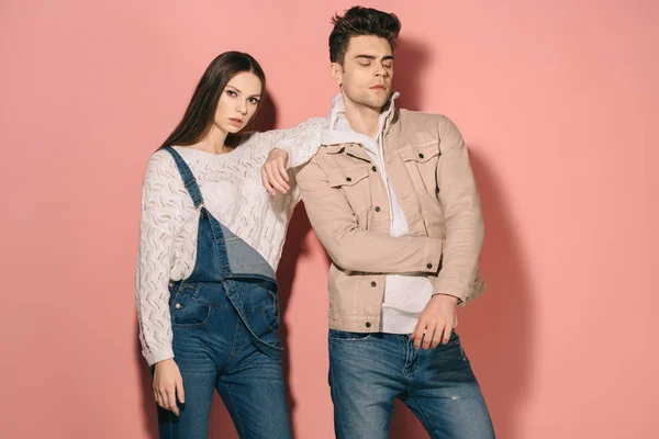 Brunette and beautiful girlfriend in denim overalls and handsome boyfriend on pink background — Stock Photo