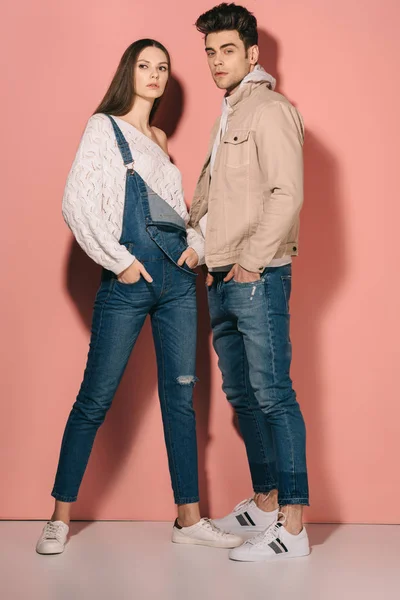 Brunette and beautiful girlfriend in denim overalls and handsome boyfriend with hands in pockets — Stock Photo