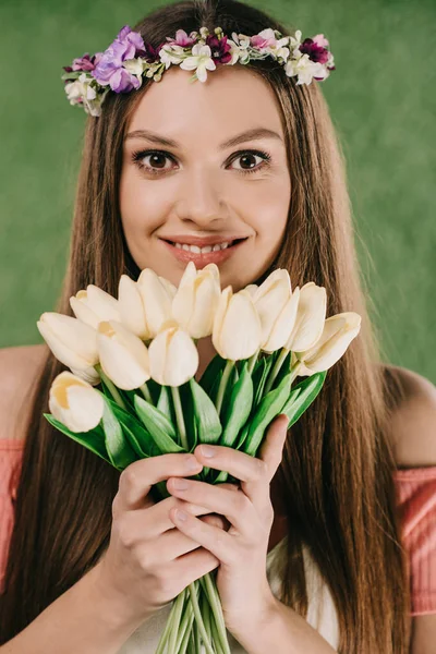 Sonriente hermosa y morena mujer en corona sosteniendo tulipanes y mirando a la cámara - foto de stock