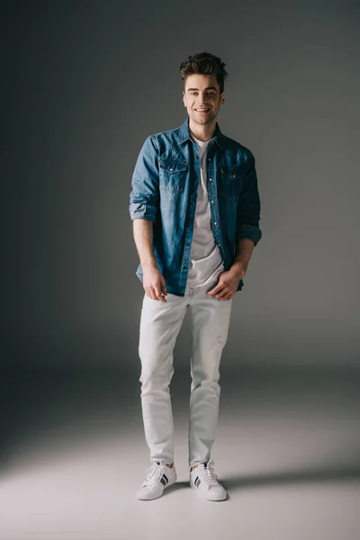 Hombre guapo sonriente en camisa de mezclilla y jeans mirando a la cámara - foto de stock