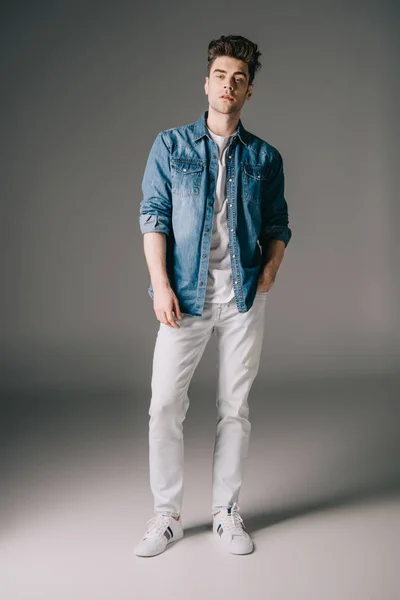 Homem bonito com mão no bolso em camisa jeans e jeans olhando para a câmera — Fotografia de Stock