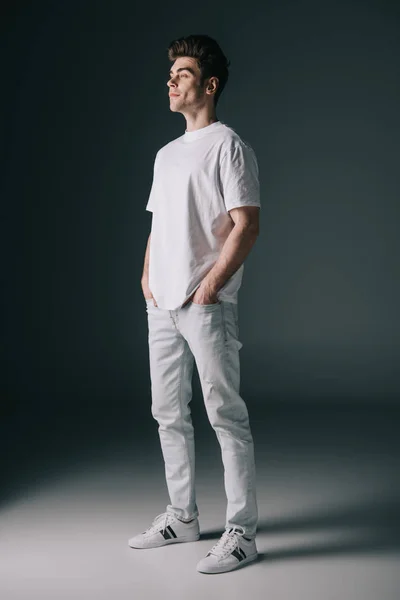 Bel homme en t-shirt blanc et jean avec les mains dans les poches détournant les yeux — Photo de stock