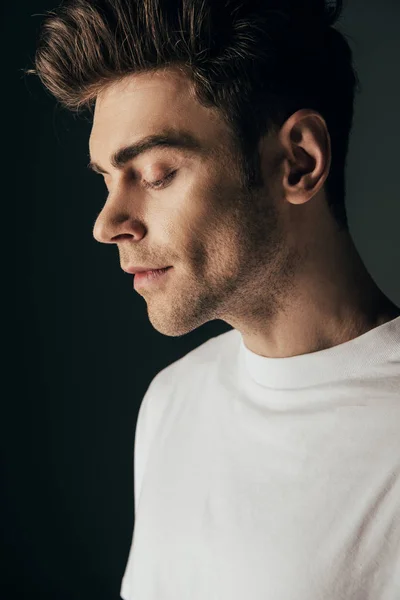 Bonito e morena homem no branco t-shirt olhando para baixo isolado no preto — Fotografia de Stock