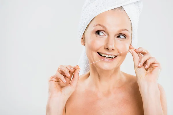 Attractive and smiling mature woman in towel brushing teeth with dental floss — Stock Photo