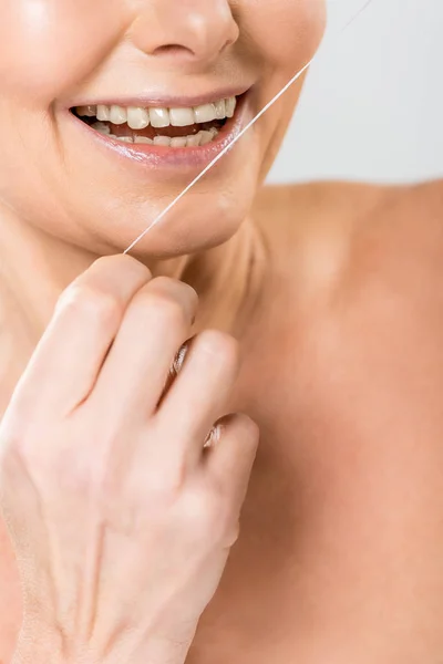 Selective focus of mature woman brushing teeth with dental floss isolated on grey — Stock Photo