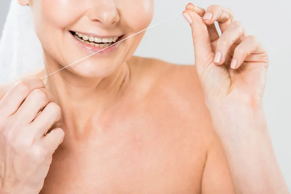 Enfoque selectivo de la mujer madura cepillarse los dientes con hilo dental aislado en gris - foto de stock