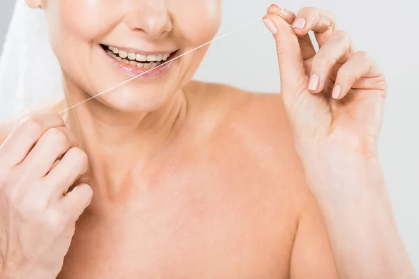 Selective focus of mature woman brushing teeth with dental floss isolated on grey — Stock Photo